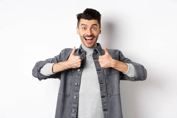 Sounds great. Excited young man showing thumbs up and smiling happy, recommending cool thing, praise nice job, standing on white background — Stock Photo, Image