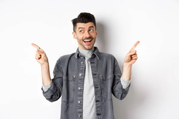 Happy stylish guy laughing and pointing sideways, showing two choices, demonstrate promo offers and smiling, standing against white background — Stock Photo, Image