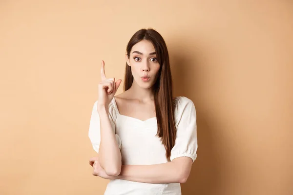 Chica creativa lanzando una idea, levantando el dedo en gesto eureka, diciendo su plan, tener una sugerencia o solución, de pie en vestido sobre fondo beige — Foto de Stock
