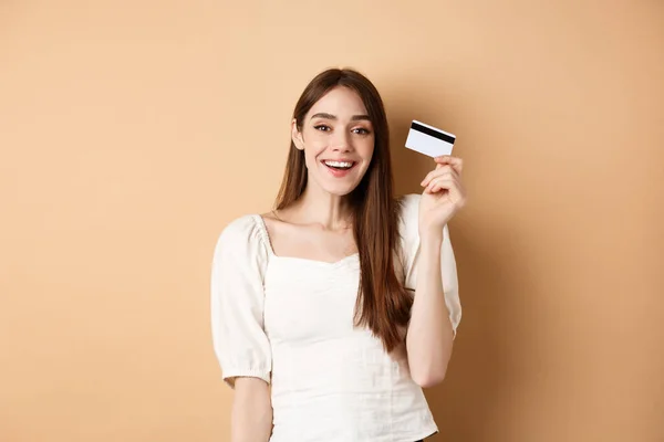 Joven alegre consiguió su tarjeta de crédito de plástico y sonriendo satisfecho, de pie satisfecho sobre fondo beige — Foto de Stock