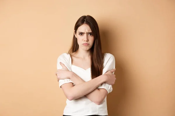 Beledigde vrouw knuffelen zichzelf en fronsen boos, gevoel timide en defensief, staan op beige achtergrond — Stockfoto