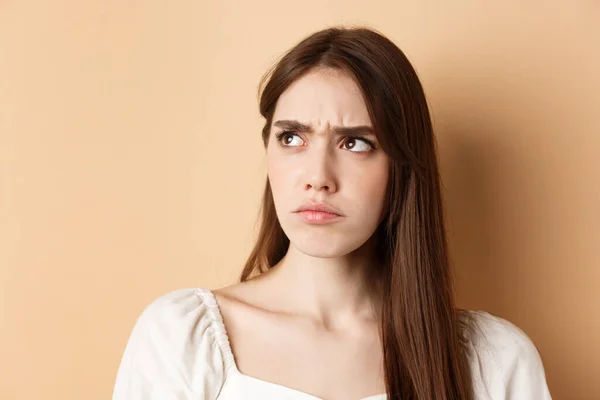 Close up of angry cute girl frowning, looking aside displeased, stare at bad thing, standing on beige background — Stock Photo, Image