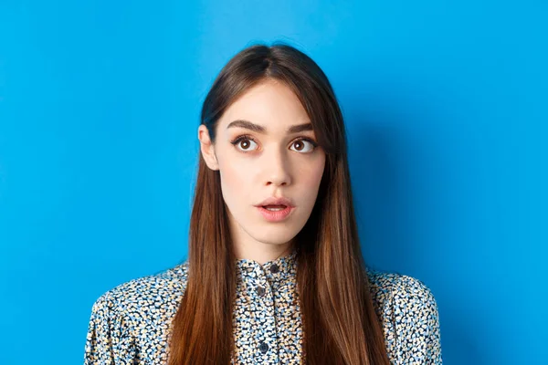 Close-up retrato de surpresa jovem com beleza natural, olhando para canto superior esquerdo e ofegante, de pé sobre fundo azul — Fotografia de Stock