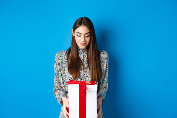 Valentines day. Surprised caucasian woman gasping amazed and looking at romantic gift, standing on blue background