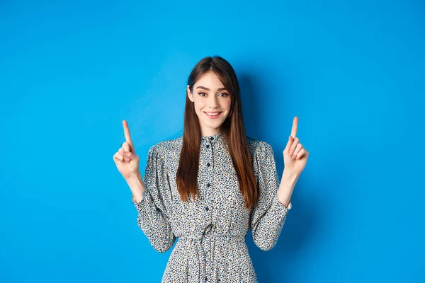 सुंदर युवा महिला लंबे बाल और विंटेज पोशाक के साथ, मुस्कुराते हुए और उंगलियों को ऊपर इंगित करते हुए, नीले पृष्ठभूमि पर विज्ञापन — स्टॉक फ़ोटो, इमेज