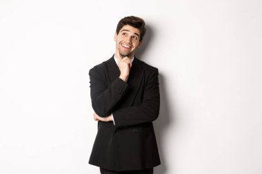 Şık bir parti elbisesi içindeki düşünceli gülümseyen adamın portresi, sol üst köşeye bakıyor ve düşünüyor, bir şeyler hayal ediyor, beyaz arka planda duruyor.