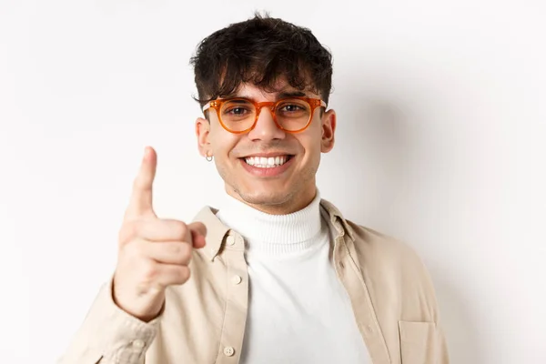 Close-up de homem bonito sorte em óculos, sorrindo e apontando o dedo para a câmera, elogiando algo bom, de pé sobre fundo branco — Fotografia de Stock