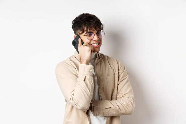 Real people concept. Handsome modern man talking on mobile phone, look aside and holding smartphone near ear, standing on white background