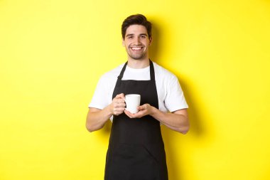 Kahve servisi yapan yakışıklı barista, fincanı getir, dostane bir gülümsemeyle siyah önlük içinde dur.