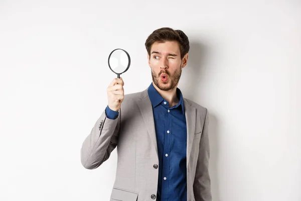 Excited funny guy in suit look through magnifying glass aside, checking out awesome thing, found something, white background — Stock Photo, Image