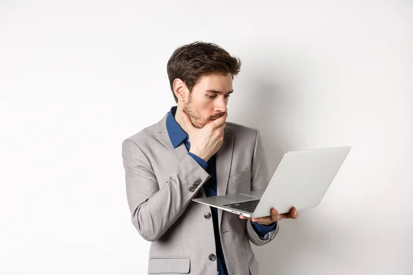 Geschokt kantoor werknemer in pak kijken bezorgd op laptop scherm, problemen op het werk, staande op witte achtergrond — Stockfoto