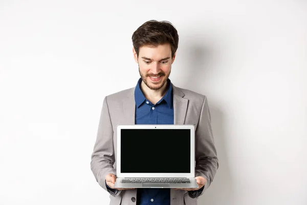 Красивый кавказский бизнесмен в костюме показывает пустой экран ноутбука, демонстрирует промо, стоя на белом фоне — стоковое фото