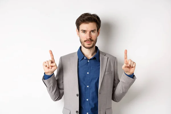 Serious businessman with beard wearing suit, pointing fingers up, look here gesture, advertising on white background — Stock Photo, Image