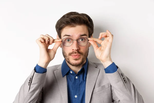 Close-up de homem bonito em terno tentando colocar novos óculos, de pé sobre fundo branco — Fotografia de Stock