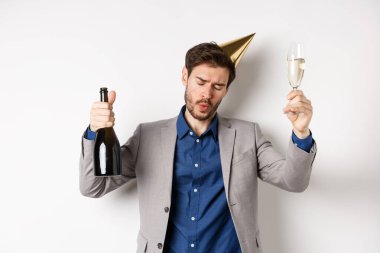 Kutlama ve tatil konsepti. Doğum günü şapkası ve takım elbisesiyle partide dans eden sarhoş adam, şampanya kadehi kaldıran, etkinlikte eğlenen, beyaz arka plan