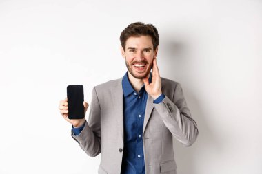 E-ticaret ve online alışveriş konsepti. Takım elbiseli mutlu adam boş akıllı telefon ekranı gösteriyor ve gülüyor, beyaz arka planda duruyor.