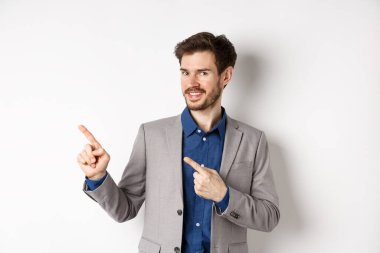 Gri takım elbiseli yakışıklı iş adamı logoyu işaret ediyor, reklamlara davet ediyor, beyaz arka planda duruyor.