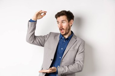 Takım elbiseli yakışıklı bir satıcı, büyük kar elde ediyor, kameraya hevesle gülümsüyor, beyaz arka planda duruyor.