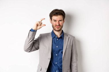 Hayal kırıklığına uğramış işadamı, küçük boyutlarda ve buruşuk suratlı üzgün, az gelirli, beyaz arka planda hoşnutsuz duruyor.