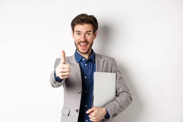 Goed gedaan. Gelukkig glimlachende zakenman in pak met laptop, duim omhoog om u te prijzen, mooi werk gebaar, staande op witte achtergrond — Stockfoto