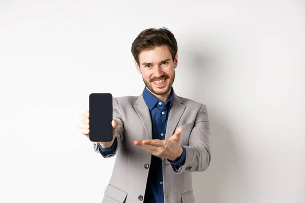 전자 상거래와 온라인 쇼핑 컨셉이야. 여기있어요. 유쾌 한 세일즈맨이 휴대폰으로 프모를 보여 주며 빈 스마트폰 화면, 흰색 배경을 보여 주고 있다 — 스톡 사진