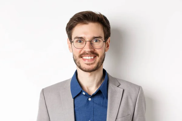 Close-up de belo jovem trabalhador de escritório em óculos e terno sorrindo para a câmera, olhando feliz no fundo branco — Fotografia de Stock