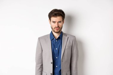 Üzgün adam somurtuyor, takım elbise giyiyor, haksız bir şey hissediyor, beyaz arka plana karşı çocuksu duruyor.