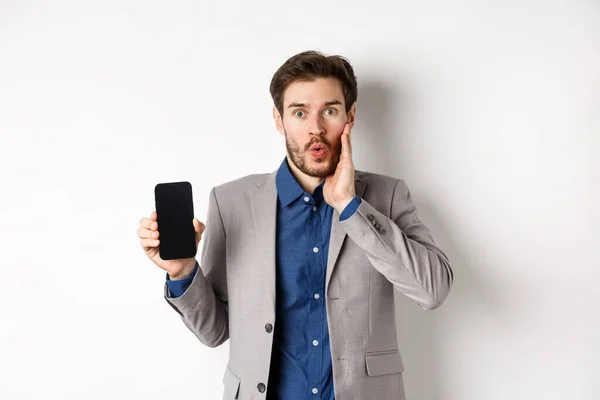 E-handel och e-handel. Spännande man kippar förvåna och visar tom smartphone skärm, bär kostym, vit bakgrund — Stockfoto