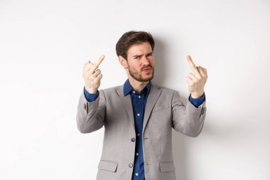 Rude businessman in suit showing middle finger, fuck you gesture, look annoyed and pissed-off, standing on white background