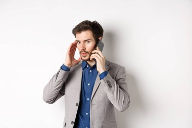 İş adamı telefonla konuşuyor ve kulaklarını kapatıyor, yüksek sesle çağrı alıyor, arayanı duymuyor, beyaz arka planda duruyor.