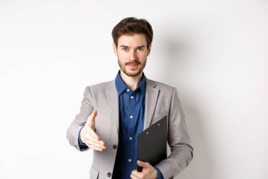 Kendine güveni tam bir işadamı. El sıkışmak için elini uzatıyor. Toplantıda iş ortaklarını selamlıyor.