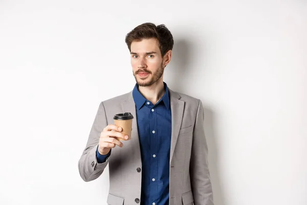 Hombre de negocios guapo en traje bebiendo café y mirando a la cámara, de pie sobre fondo blanco — Foto de Stock