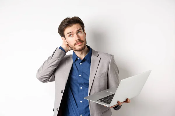 Bedachtzame zakenman krassen hoofd en kijk weg, het nemen van beslissingen tijdens het werken op laptop, staan tegen een witte achtergrond — Stockfoto