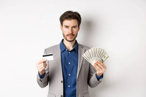 Empresário bem sucedido ganhar dinheiro, de pé em terno com notas de dólar e cartão de crédito de plástico, fundo branco — Fotografia de Stock