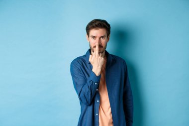 Ignorant and rude guy showing middle finger and smiling, say fuck you, standing on blue background