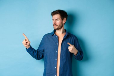 Kafkasyalı genç bir adamın görüntüsü, bir kenara bakıyor, reklamını yapıyor, mavi arka planda duruyor.