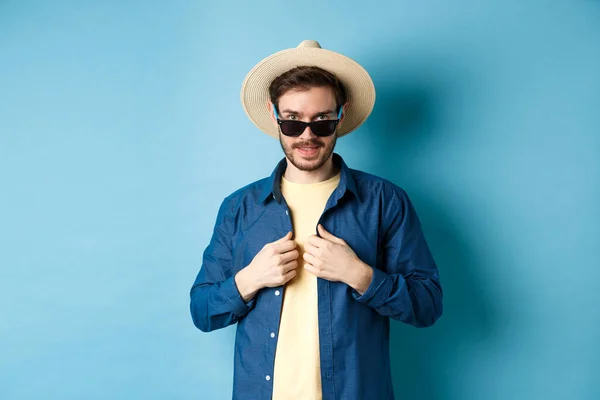 Joven guapo que se va de vacaciones, ajustando camisa, usando gafas de sol y sombrero de paja. Concepto de vacaciones de verano — Foto de Stock