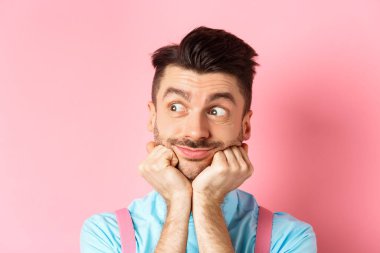 Şirin bir adamın bir şeyler hayal ettiği yakın plan, yan gözle bakmak ve bir şeyler hayal etmek, pembe arka planda durmak, ellere yaslanmış yüz, pembe arka plan..