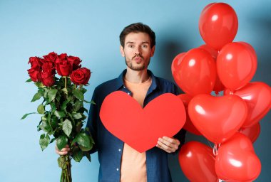 Aşık bir adam sevgililer gününü kutluyor, romantik randevuda öpüşmeyi bekliyor, kırmızı güller, kırmızı kalp ve balonlar, mavi arka planda duruyor..