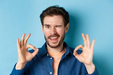 Yakışıklı, kendine güvenen, iyi jestler yapan, kalite garantisi veren, iyi bir şey öneren, mavi arka planda duran...