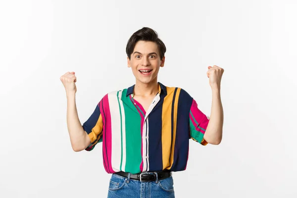 Happy young man rejoicing, clench fists and looking with satisfaction, achieve goal or win prize, standing over white background — Stock Photo, Image