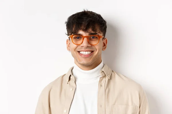 Zbliżenie przystojnego hipstera z naturalnym uśmiechem, noszącego okulary i kolczyki, szczęśliwie wyglądającego przed kamerą, stojącego na białym tle — Zdjęcie stockowe