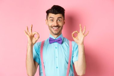 Gülümseyen, gülümseyen yakışıklı bir adam. Onaylanmış güzel jestler yapıyor. İyi seçimi övüyor, reklamları seviyor, pembe arka planda duruyor.