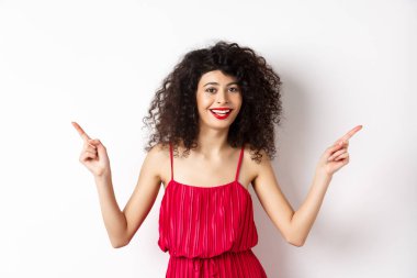 Kıvırcık saçlı, kırmızı dudaklı, gülümseyen beyaz dişli, iki tarafı gösteren, reklamları bir kenara bırakıp beyaz arka planda duran mutlu bir kadın.