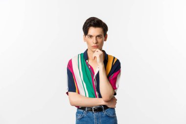 Yakışıklı ve şık bir adamın portresi kameraya düşünceli bakıyor, seçim yapıyor, sana bakmayı düşünüyor, beyaz arka planda duruyor.