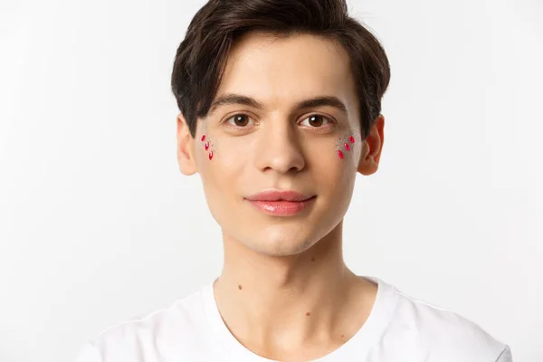 People, lgbtq and beauty concept. Close-up of happy queer guy with applied lip gloss and glitter, smiling and looking at camera, standing over white background — Stock Photo, Image