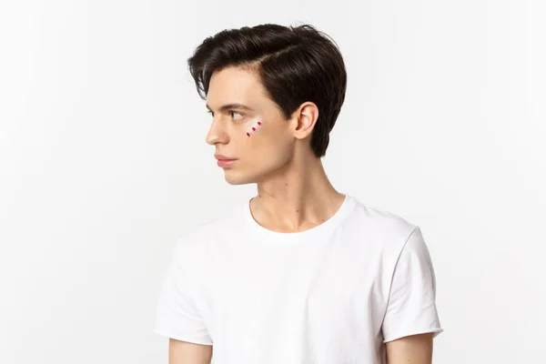 People, lgbtq community and lifestyle concept. Profile view of handsome gay man with glitter on face, looking left, standing over white background — Stock Photo, Image