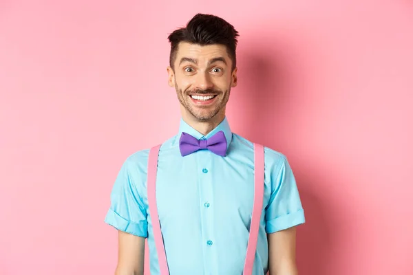 Щасливий молодий чоловік з вусами, посміхаючись на камеру, виглядає схвильованим і веселим, стоїть на рожевому тлі в сорочці і бантику — стокове фото