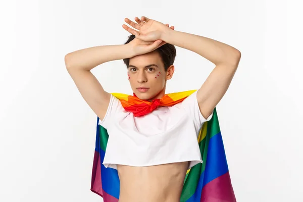 Bonito gay homem com glitter no rosto vestindo safra superior e arco-íris lgbt bandeira posando contra branco fundo — Fotografia de Stock