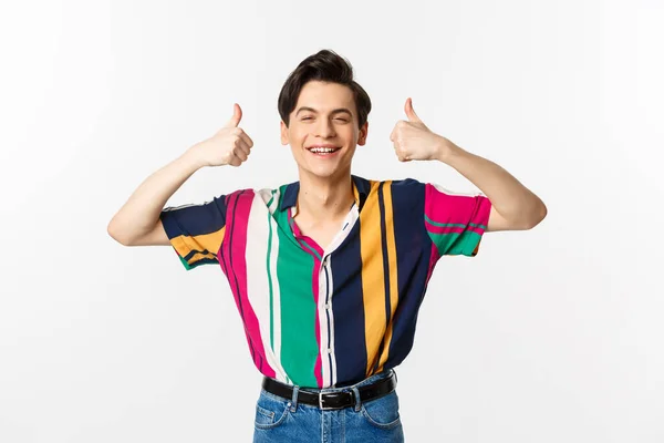 Young cheerful man smiling, showing thumbs up in approval, praise something good, standing over white background — Stock Photo, Image